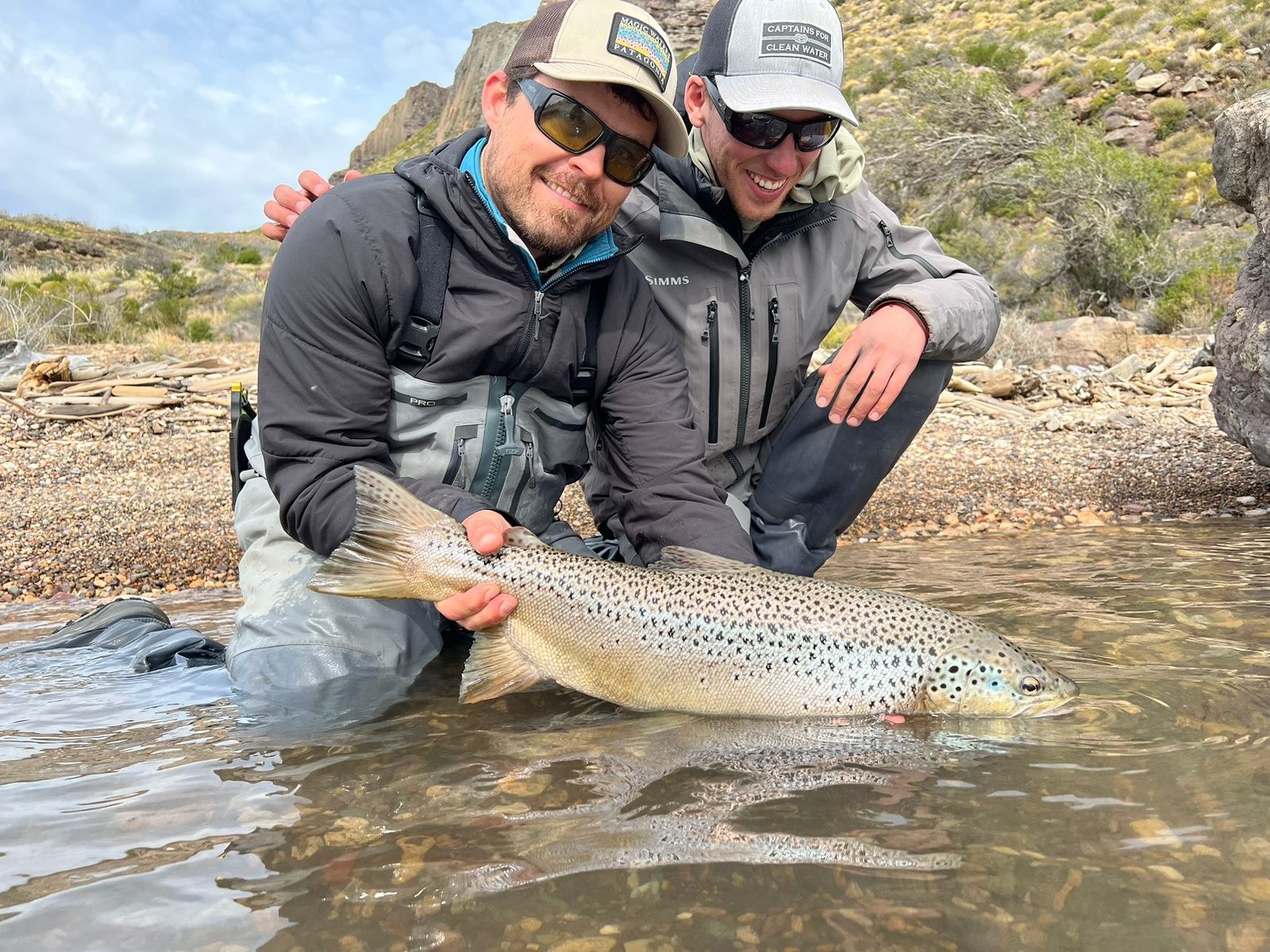 Two anglers with a silver-sided brown trout in a canyon river in Chilean Patagonia