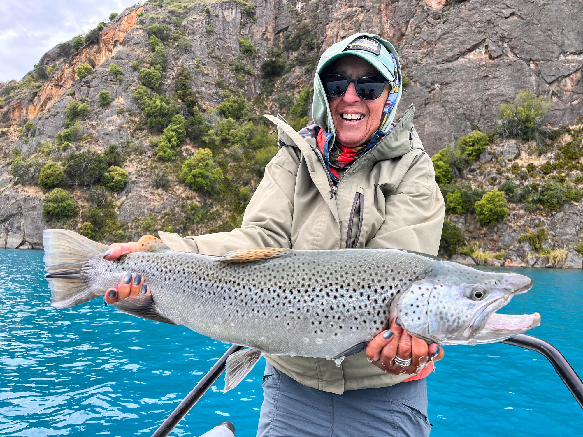 Angler with a silver-sided brown trout on turquoise water in Chilean Patagonia