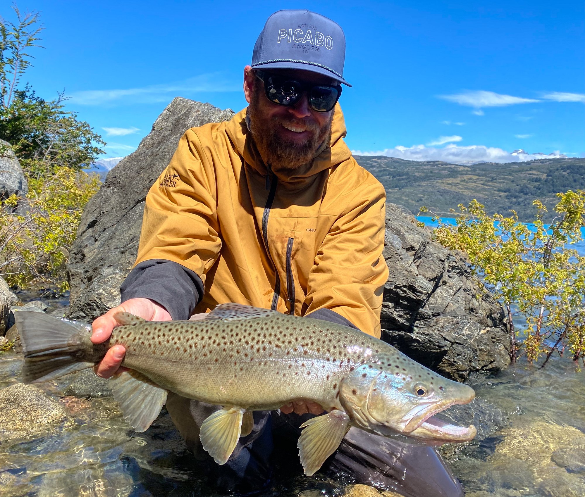 Guest in a mustard jacket holding a big brown trout in Patagonia