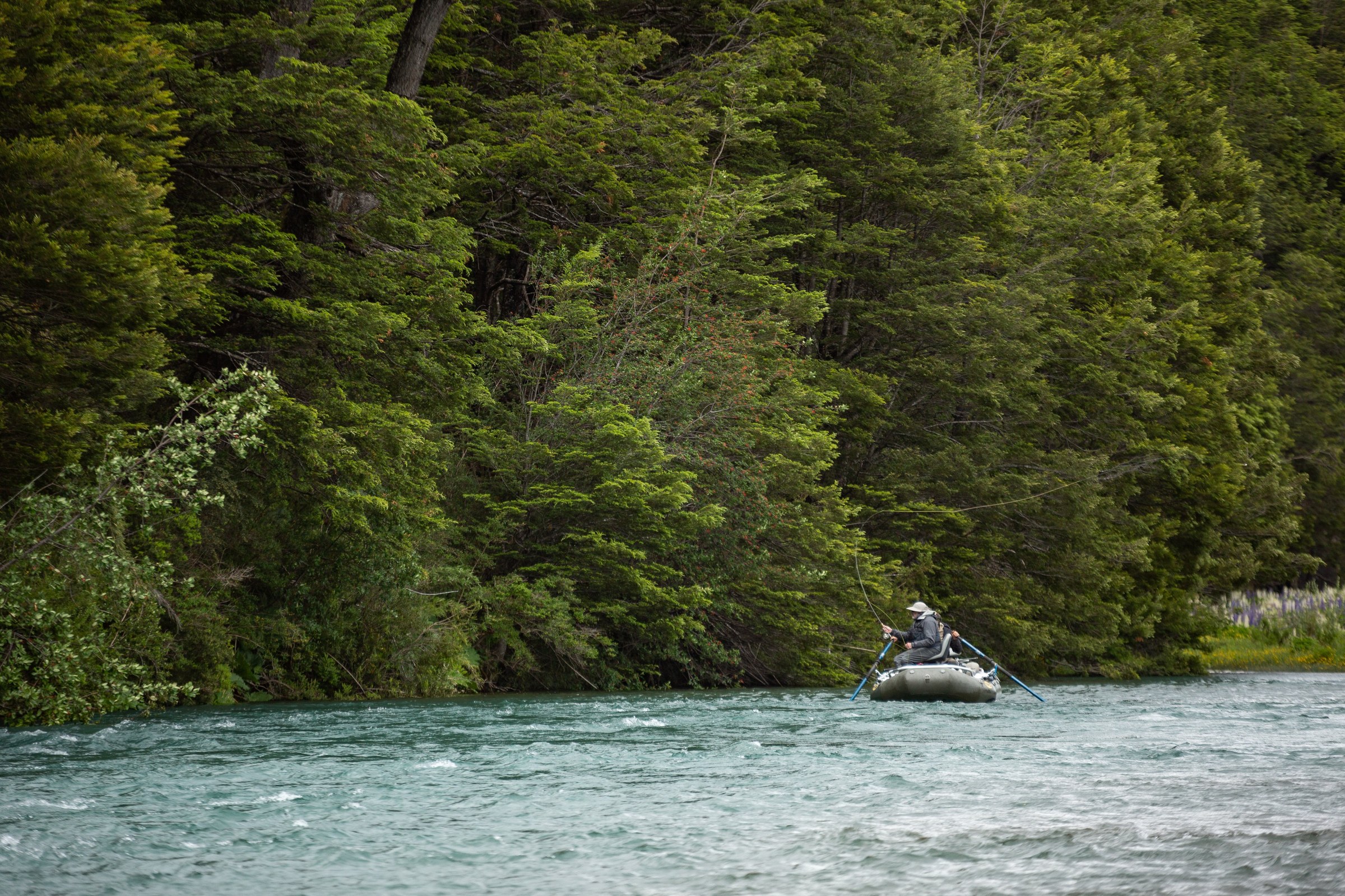 Drift boat on turquoise Patagonia water along a forested bank near Coyhaique