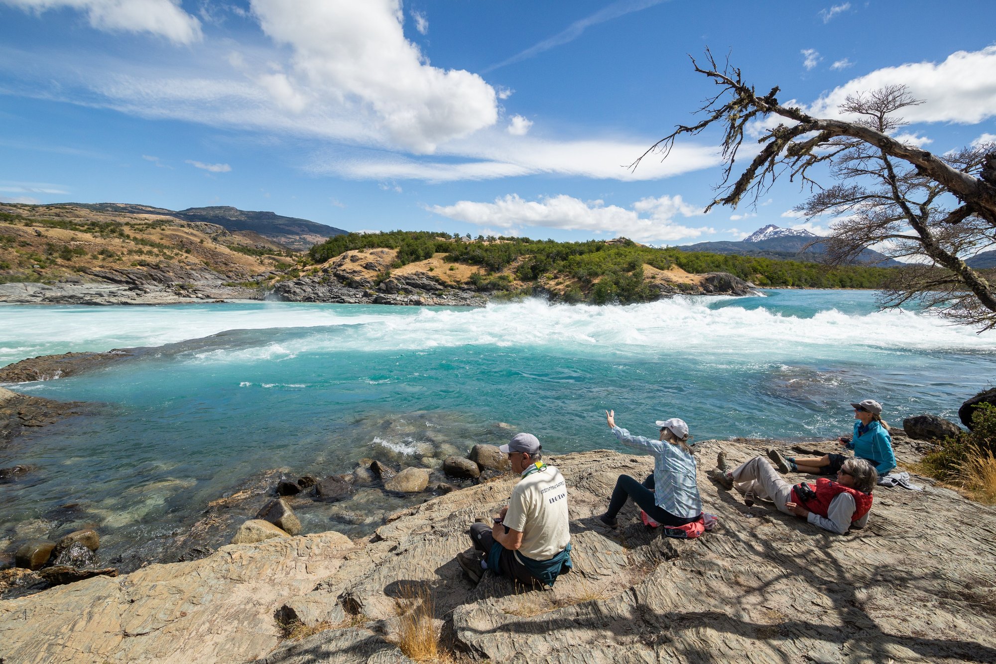 Guests resting on rocks beside a turquoise rapid on the Río Baker